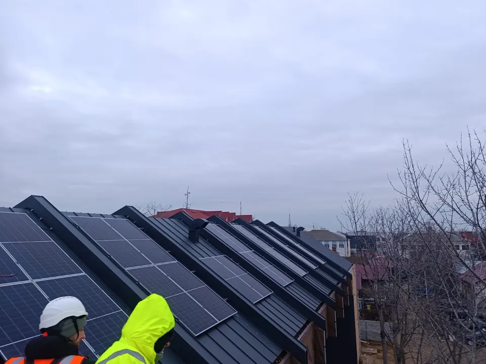 Doi montatori Intelitech lângă panouri fotovoltaice pe un acoperiș din tablă cu mai multe coame paralele
